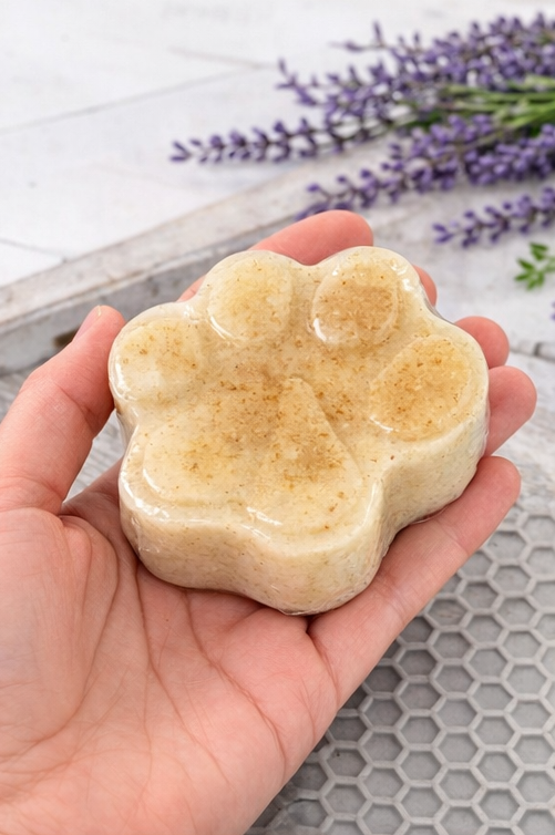 Hand holding a paw-shaped soap bar with lavender flowers in the background