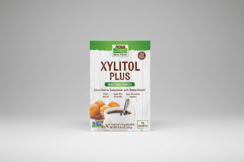Package of Xylitol Plus sweetener packets with a cup of coffee and cookies on a white background.