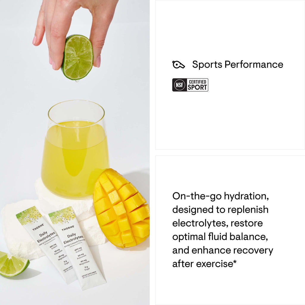Glass of yellow drink with lime and mango, with a hand adding a lime slice, on a white background.