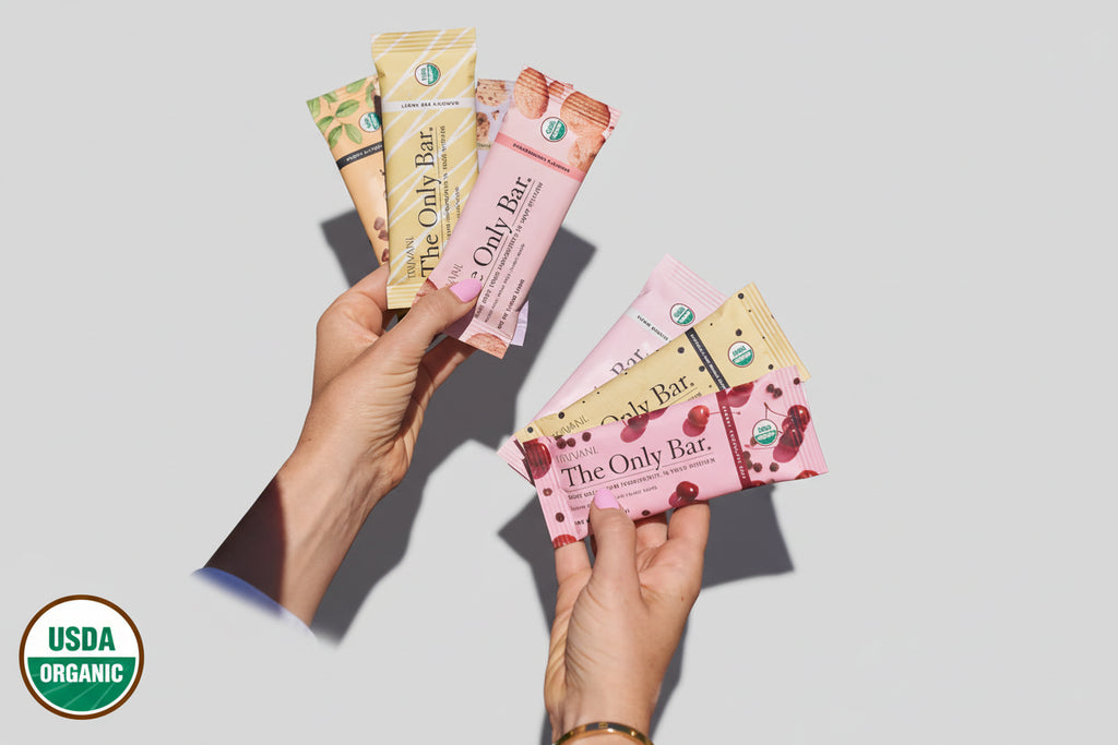 Hands holding various flavors of 'The Only Bar' with a pool background and USDA Organic logo.